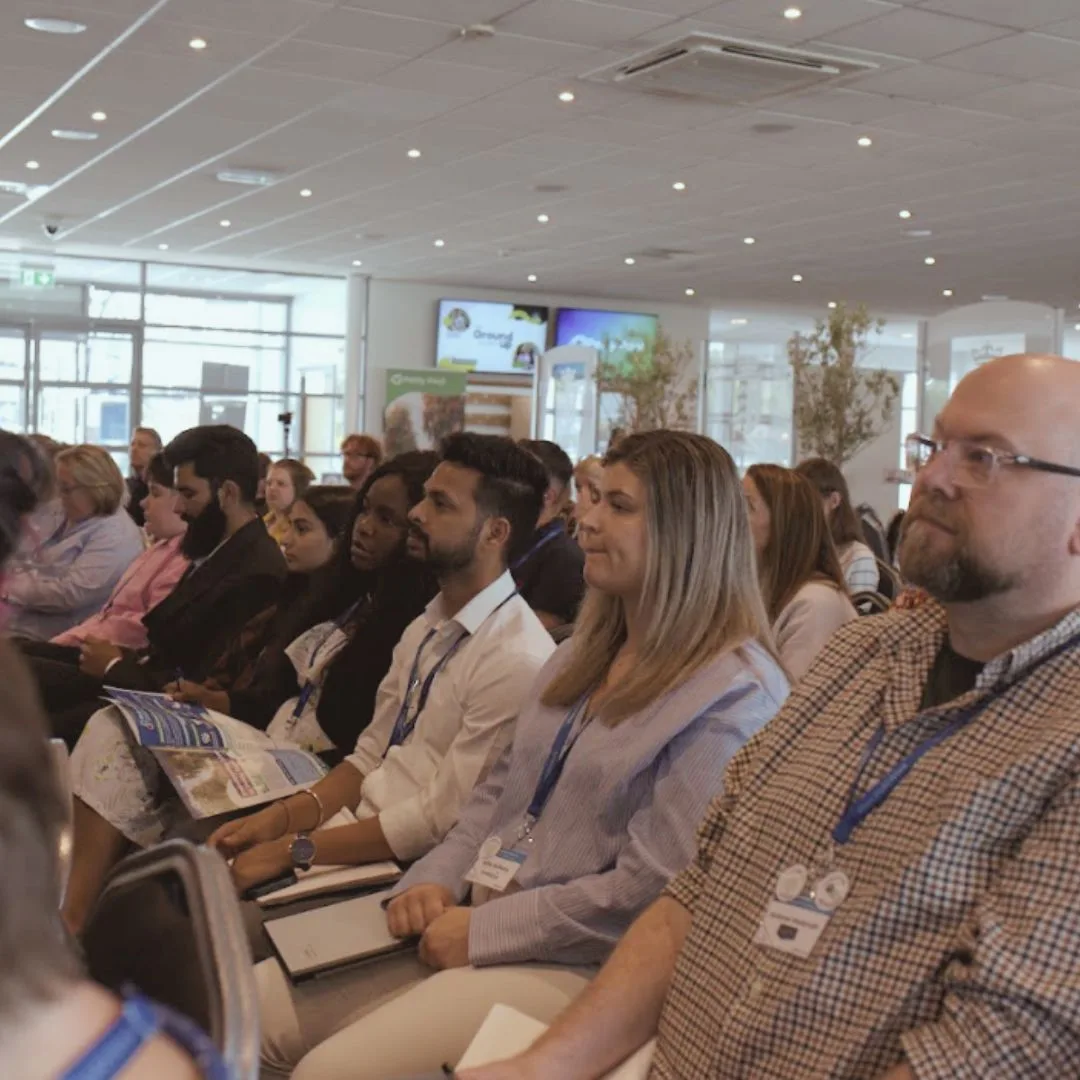 Rows of seated delegates wearing lanyards listening to a session in a large conference room
